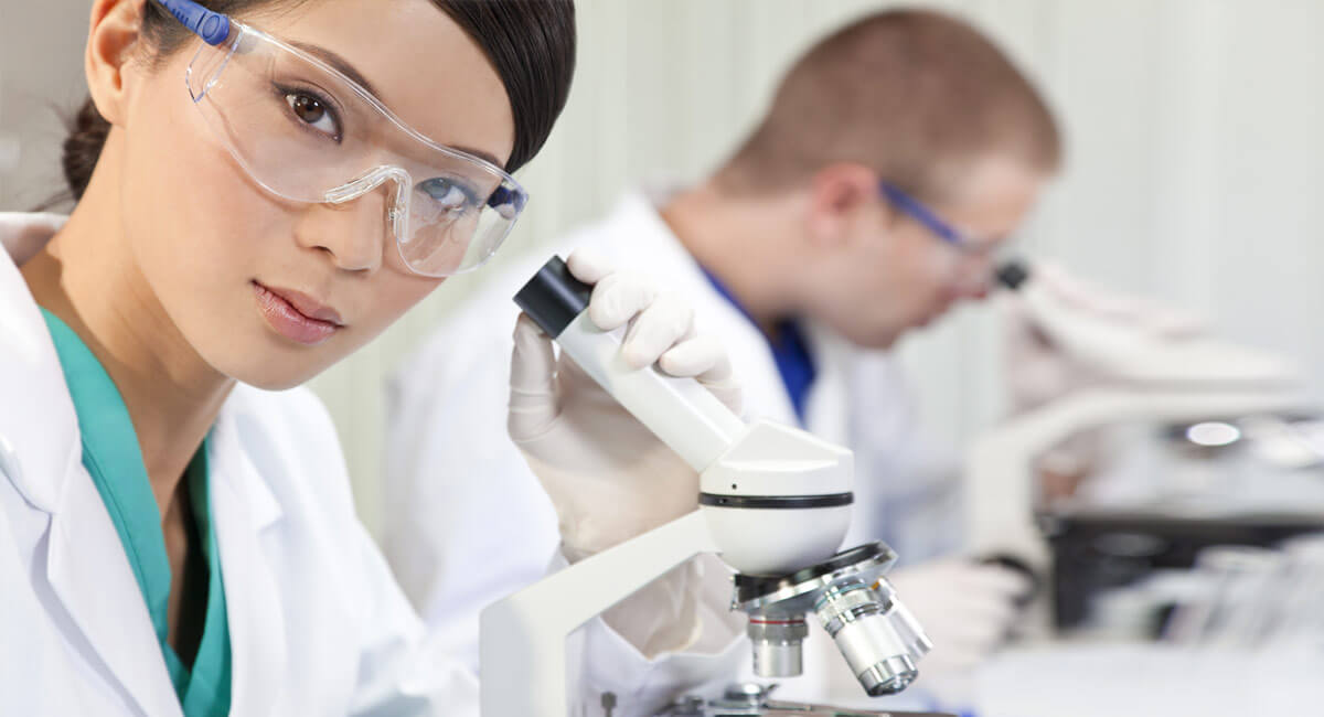 a woman in protective glasses next to the microscope